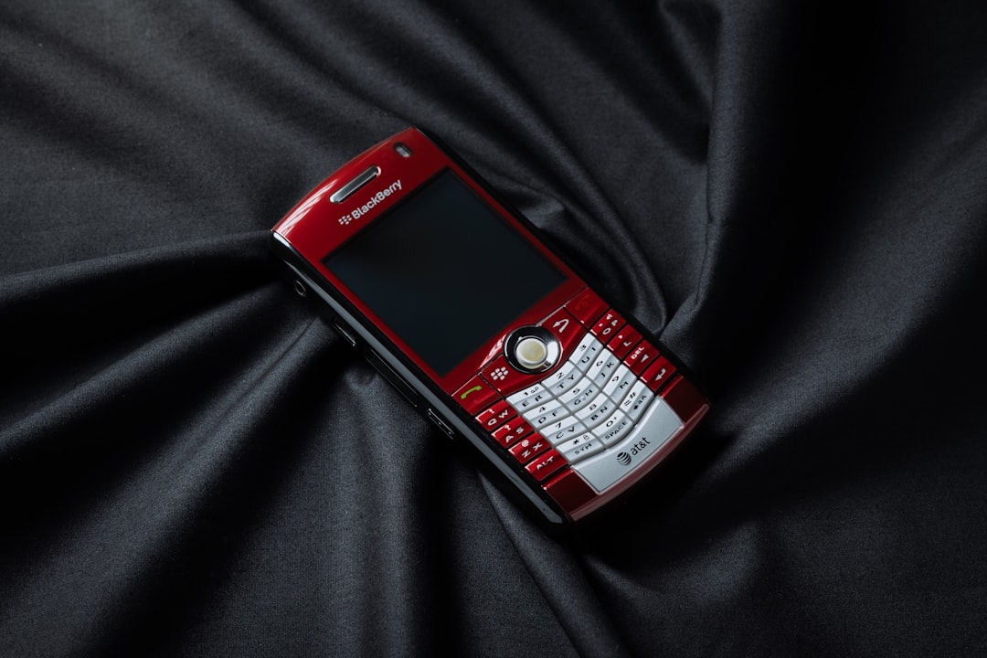 A red and white cell phone laying on a black cloth